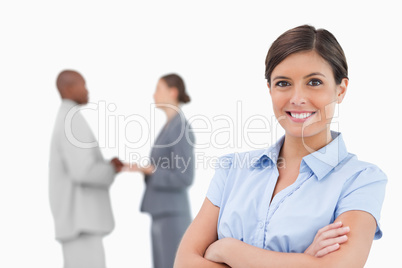 Smiling businesswoman with arms crossed and colleagues behind he