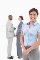 Smiling businesswoman with talking co-workers behind her