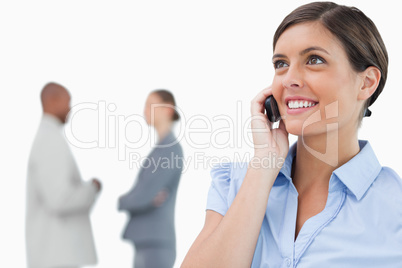 Smiling businesswoman with mobile phone and associates behind he