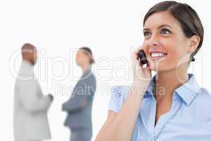 Smiling businesswoman with mobile phone and associates behind he