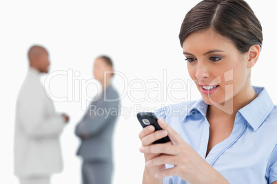 Businesswoman reading text message with associates behind her