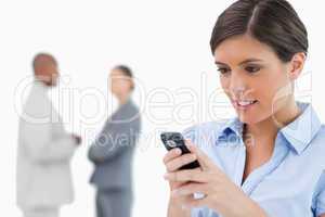 Businesswoman reading text message with associates behind her