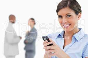 Smiling saleswoman holding mobile phone with colleagues behind h