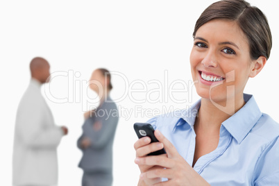 Smiling saleswoman with mobile phone and associates behind her