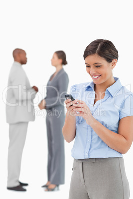 Businesswoman looking at cellphone with associates behind her