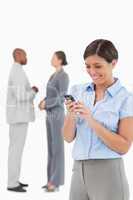 Businesswoman looking at cellphone with associates behind her