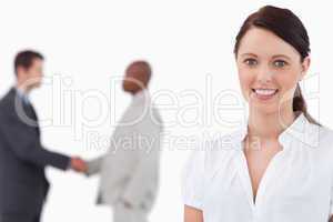 Smiling saleswoman with hands shaking trading partners behind he