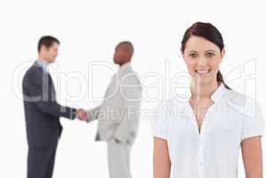 Smiling businesswoman with hand shaking trading partners behind