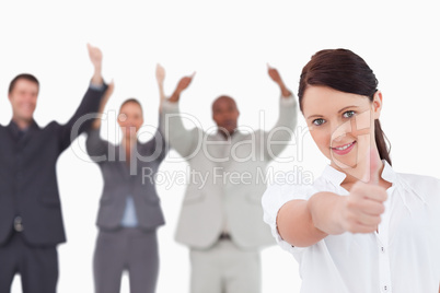 Businesswoman with cheering colleagues behind her giving thumb u