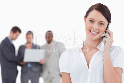 Smiling businesswoman with mobile phone and co-workers behind he