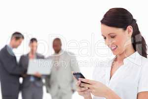 Businesswoman writing text message with colleagues behind her