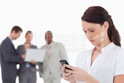 Saleswoman reading text message with colleagues behind her