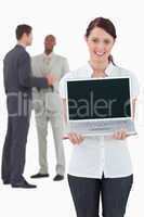 Businesswoman showing laptop with colleagues behind her