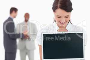 Businesswoman showing laptop with associates behind her