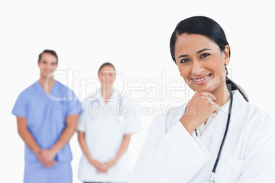 Smiling doctor in thinkers pose with colleagues behind her