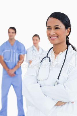 Smiling doctor with arms folded and colleagues behind her