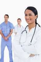 Smiling doctor with arms folded and colleagues behind her