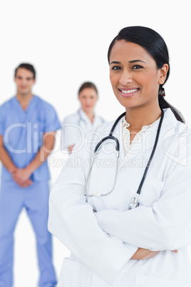 Smiling doctor with arms folded and staff behind her