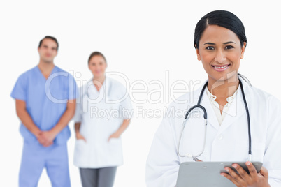 Smiling doctor with clipboard and staff behind her