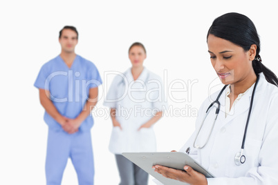 Doctor taking notes with staff behind her
