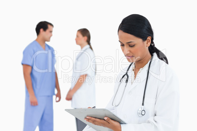 Doctor taking notes with talking staff members behind her