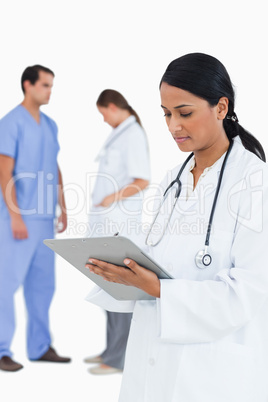 Doctor taking notes with staff members behind her