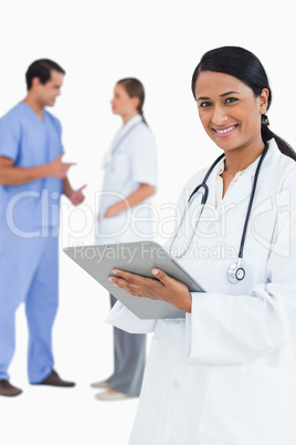 Smiling doctor with clipboard and staff members behind her