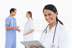 Smiling doctor with clipboard and colleagues behind her