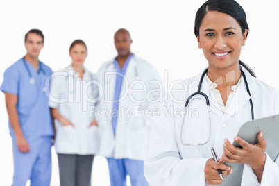 Smiling doctor with clipboard and members of staff behind her