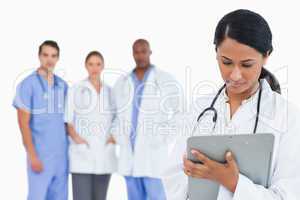 Female doctor taking notes on clipboard with staff members behin
