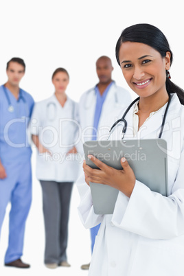 Smiling female doctor with clipboard and staff behind her