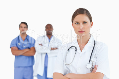 Female doctor with folded arms and male colleagues behind her