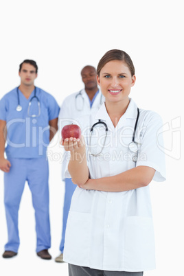 Smiling doctor with apple and colleagues behind her