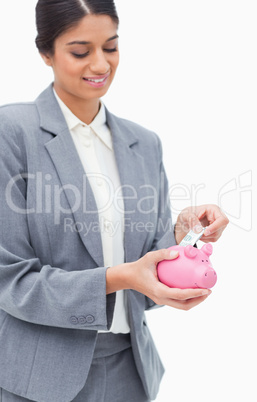 Smiling bank employee putting bank note into piggy bank