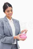 Smiling bank assistant putting bank note into piggy bank