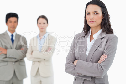 Confident saleswoman with arms folded and colleagues behind her