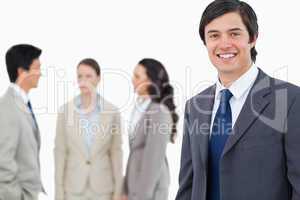 Smiling young businessman with talking associates behind him