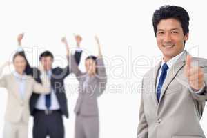 Businessman giving thumb up while getting celebrated