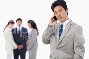 Serious businessman on cellphone with team behind him