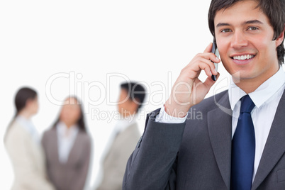 Smiling salesman on his cellphone with team behind him