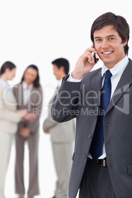 Smiling salesman on cellphone with team behind him