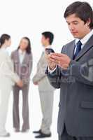 Salesman reading text message on cellphone with team behind him