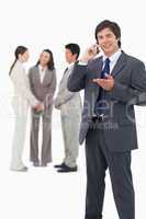 Salesman talking on cellphone with team behind him