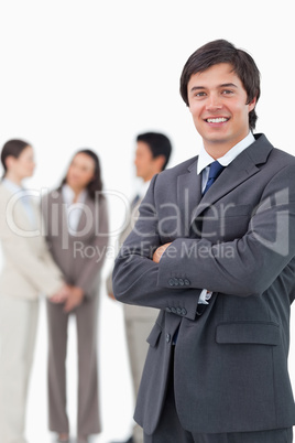 Smiling salesman with arms crossed and team behind him