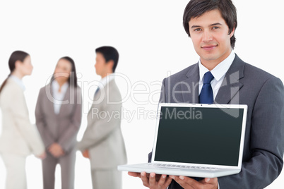 Salesman showing laptop screen with colleagues behind him