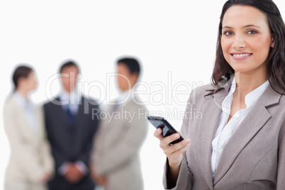 Smiling saleswoman holding cellphone with team behind her