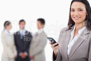 Smiling saleswoman holding cellphone with team behind her