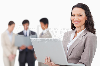 Smiling saleswoman with laptop and colleagues behind her