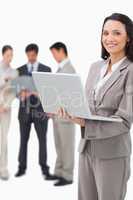 Smiling saleswoman with notebook and colleagues behind her