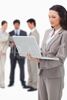 Saleswoman standing with laptop and colleagues behind her
